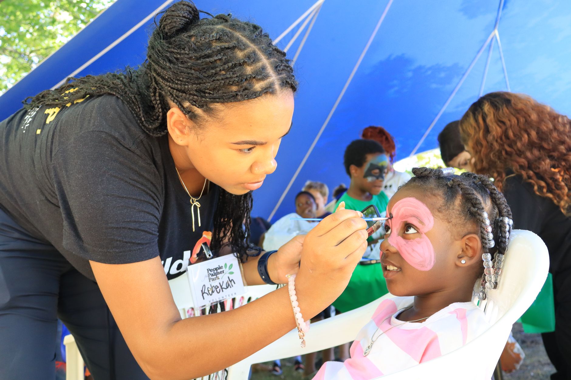 A young woman paints a child's face at an outdoor festival, enhancing community joy and creativity.