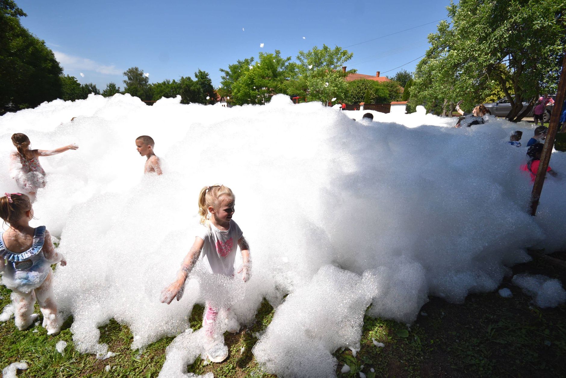 A lively scene of children playing in an outdoor foam party, enjoying a sunny day.