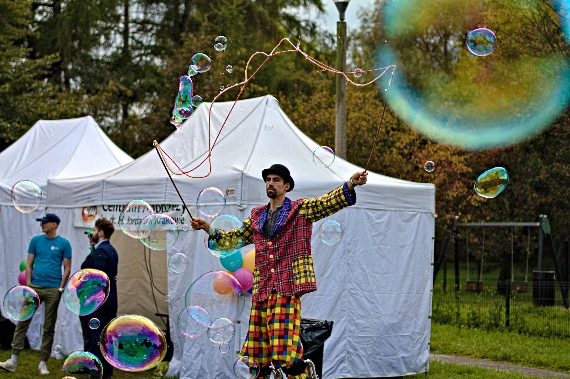 Colorful street performer creating large bubbles in a park in Kraków, Poland.