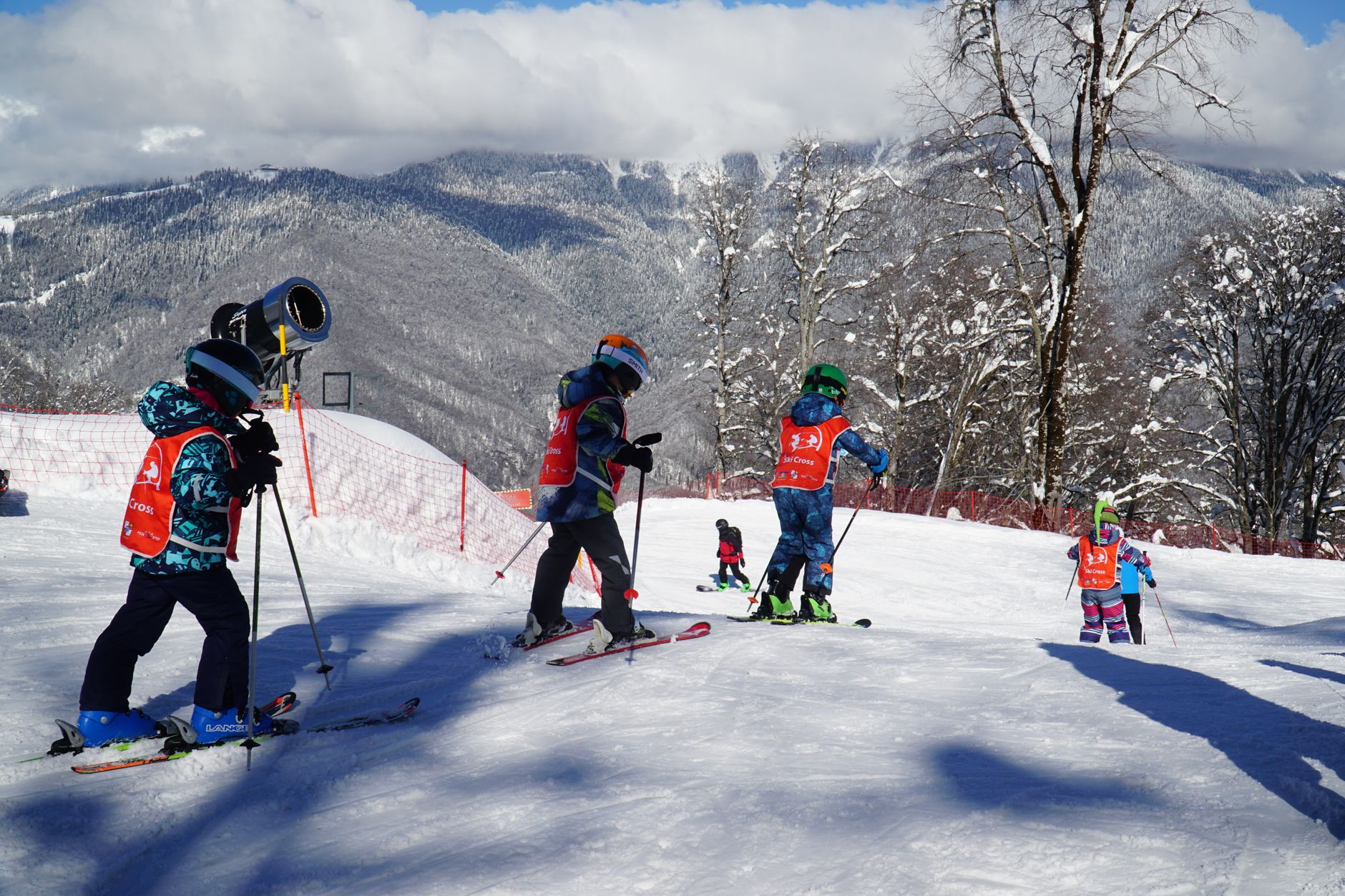 Group of children learning to ski on a snowy slope in Adlerskiy, Russia, under clear winter skies.