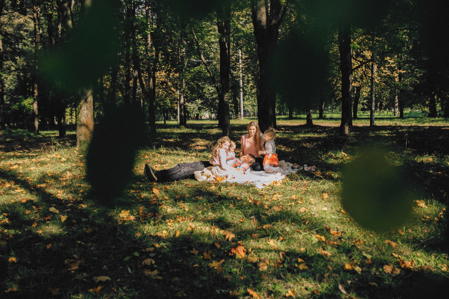 A joyful family picnic in a sunny forest park, surrounded by lush greenery and fallen leaves.