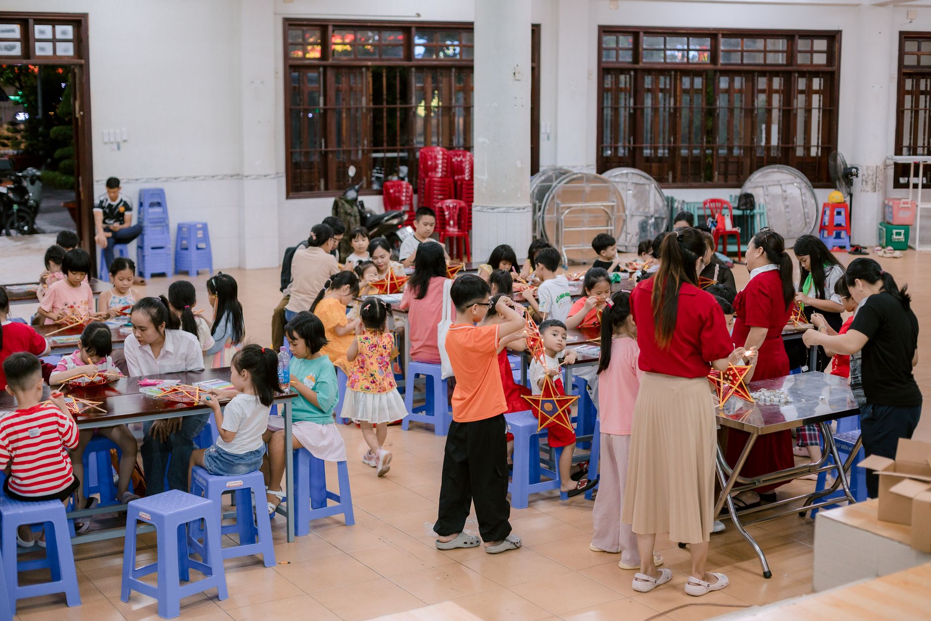 Children engaging in a creative indoor activity making lanterns with adults supervising.