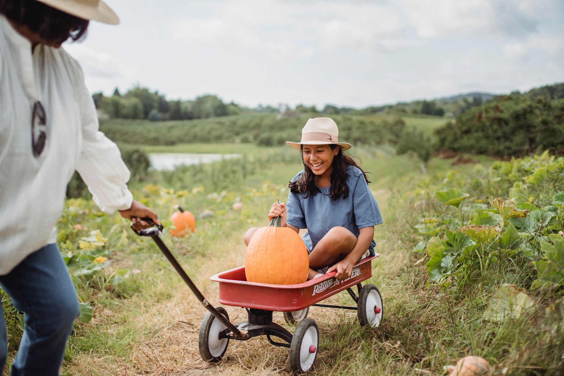 A girl riding in a wagon with a pumpkin on a lush green farm.