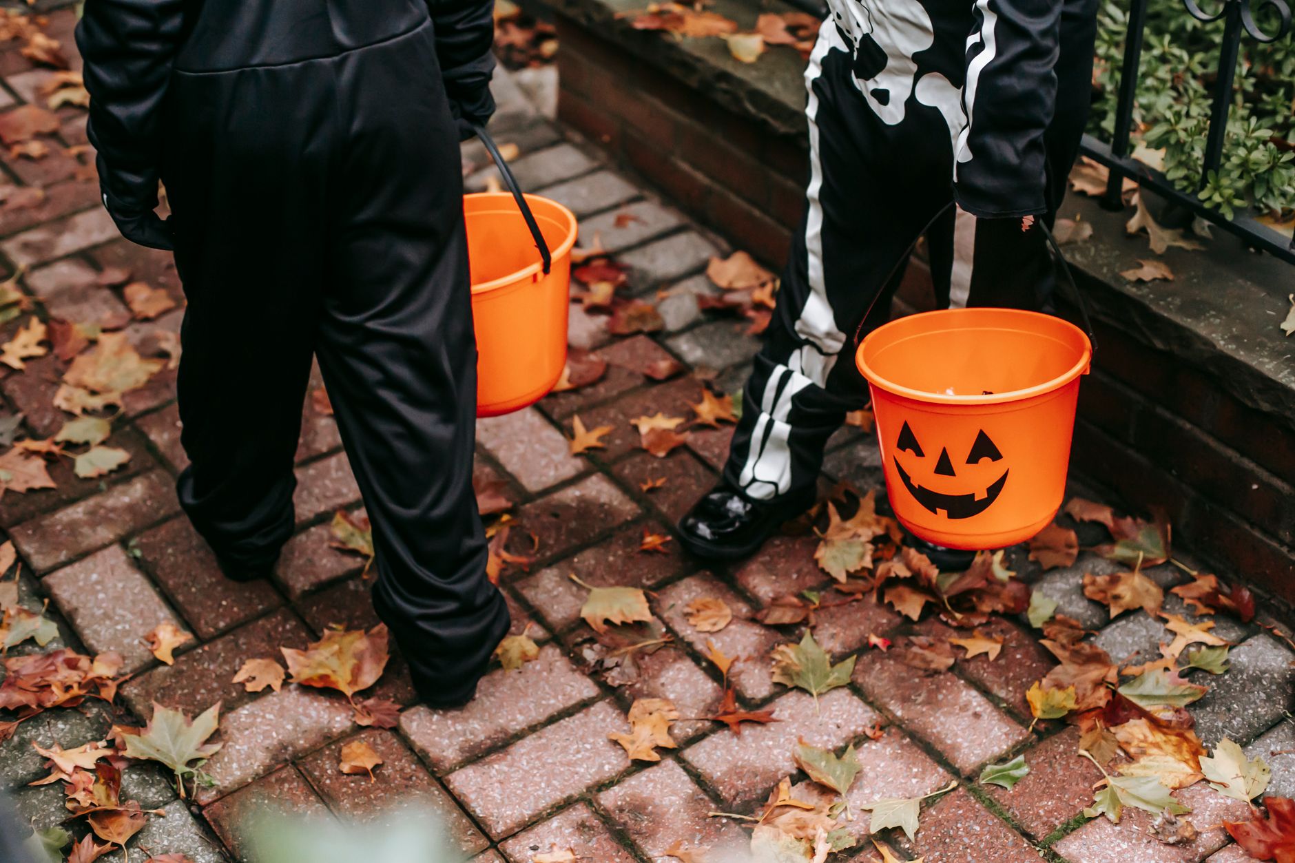 Crop unrecognizable children in black skeleton costumes with orange buckets trick or treating in Halloween in day