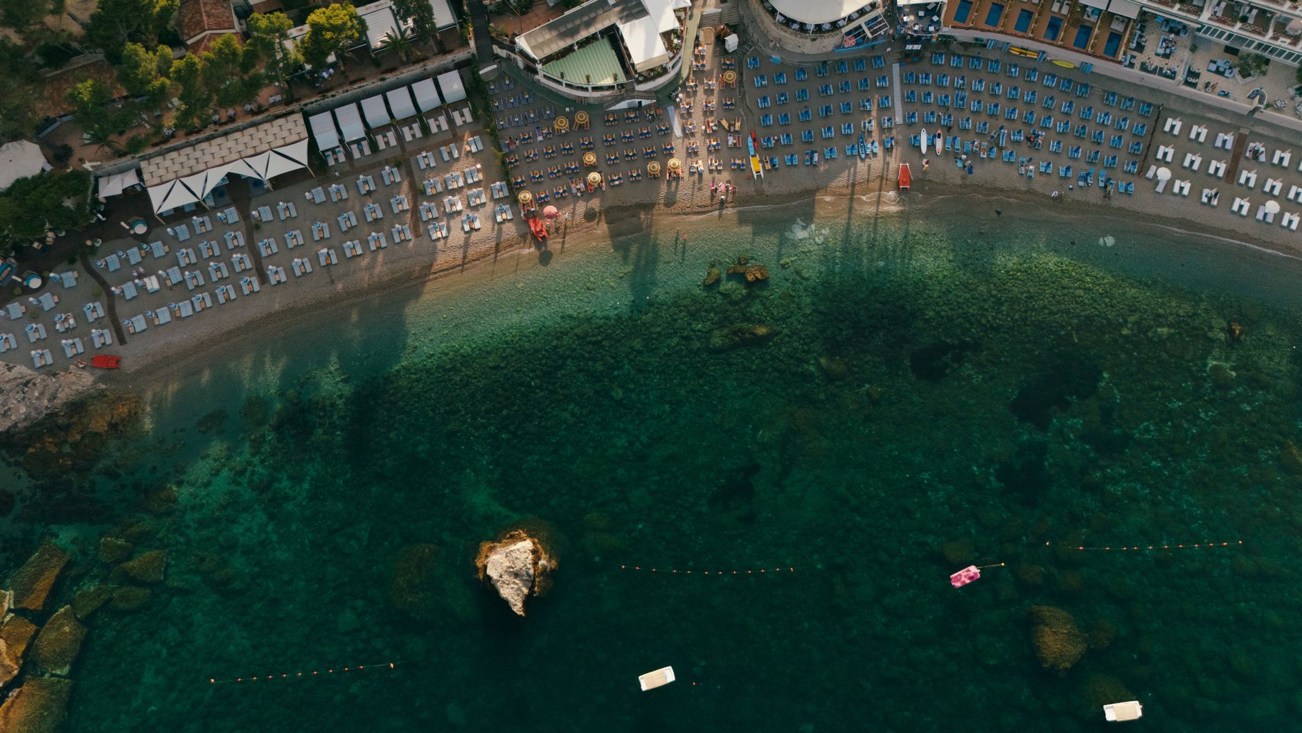 Drone shot capturing a picturesque beachfront resort with sunbeds and clear sea water.