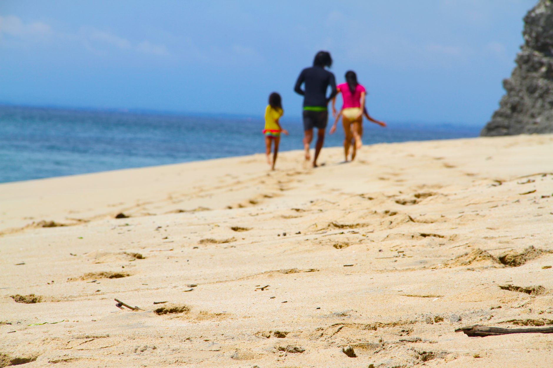 A family strolls along a sandy beach under a bright summer sky, enjoying leisure and nature.