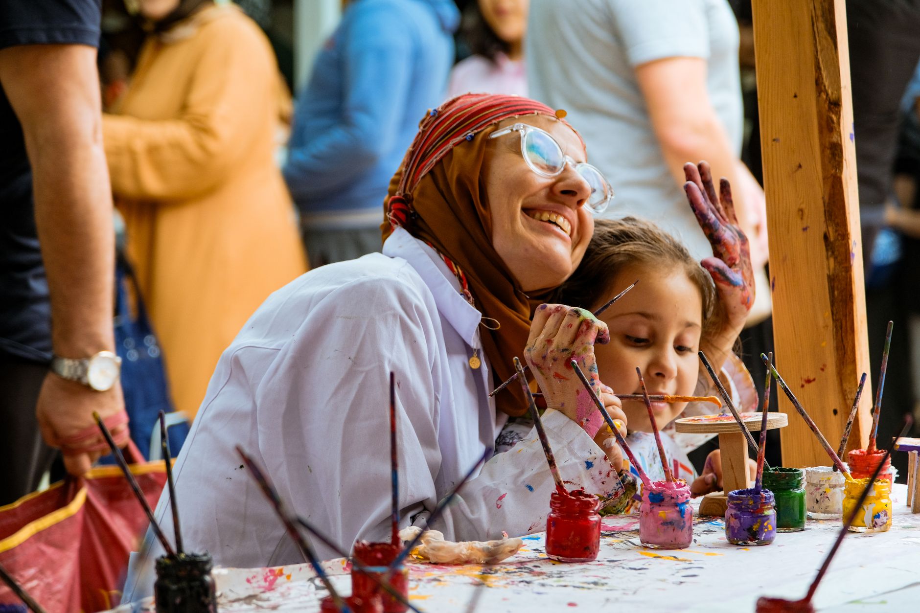 A mother and child joyfully paint together at an outdoor art workshop.