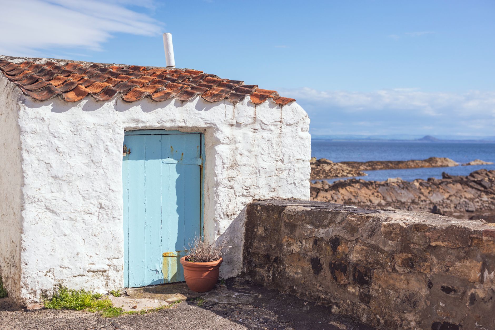 Charming white seaside cottage with a blue door, set against the coastal landscape of Pittenweem, Scotland.