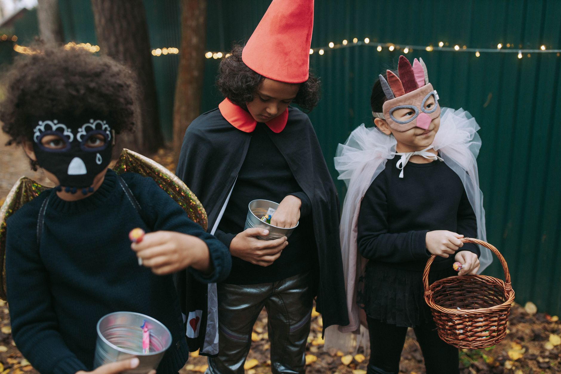 Three children in creative Halloween costumes collect candy outdoors during trick-or-treat.